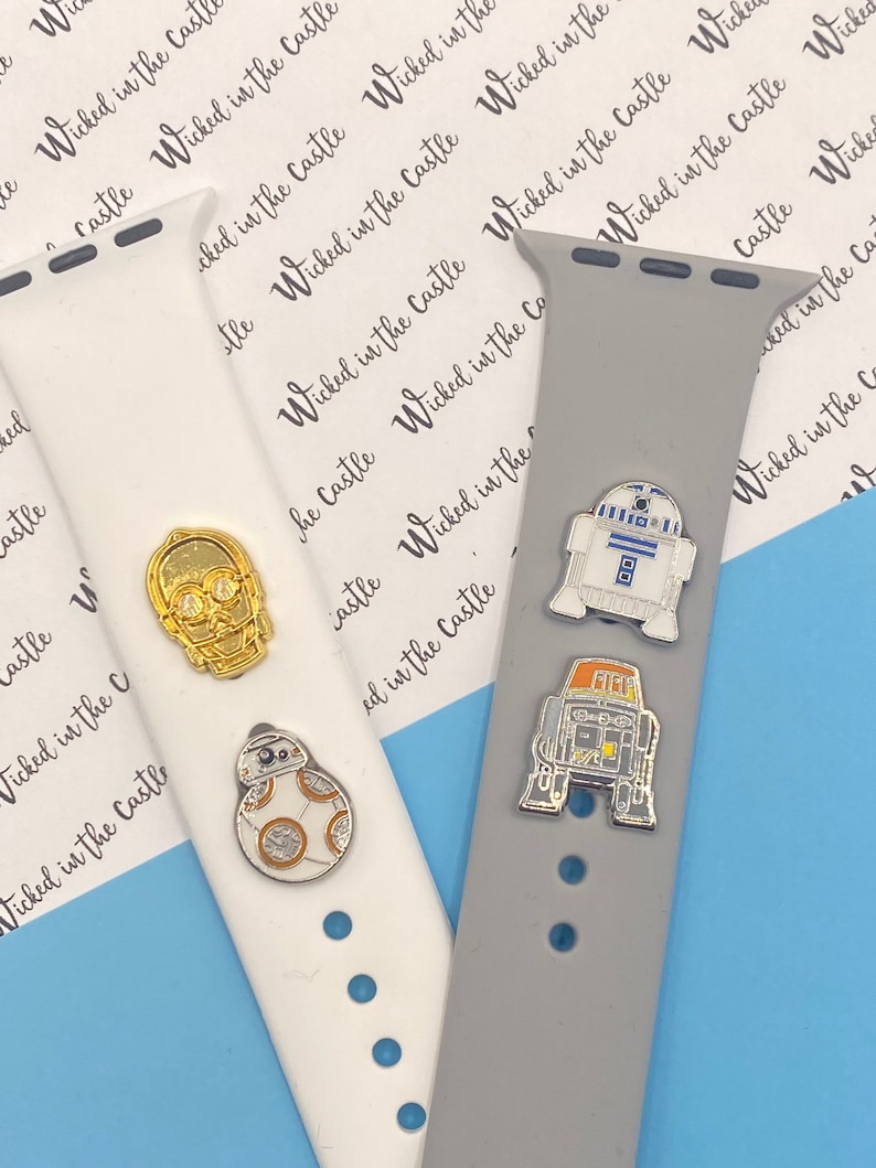 May include: Three different Apple Watch bands with Star Wars character charms. The bands are white, gray, and black. The charms are of R2-D2, C-3PO, and a Stormtrooper.