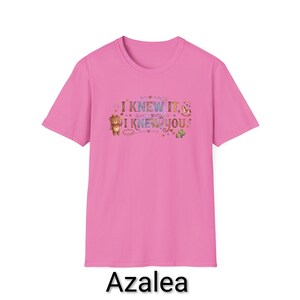 Puede incluir: Una camiseta de manga corta de color rosa brillante con un estampado gr&aacute;fico en el pecho. El dise&ntilde;o incluye el texto "I KNEW IT, I KNEW YOU" en una fuente colorida, rodeado de peque&ntilde;as ilustraciones de un oso de peluche, un caballito balanc&iacute;n y un cactus.