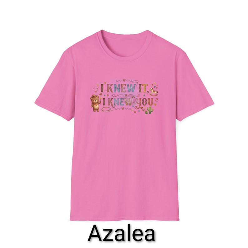Puede incluir: Una camiseta de manga corta de color rosa brillante con un estampado gr&aacute;fico en el pecho. El dise&ntilde;o incluye el texto "I KNEW IT, I KNEW YOU" en una fuente colorida, rodeado de peque&ntilde;as ilustraciones de un oso de peluche, un caballito balanc&iacute;n y un cactus.