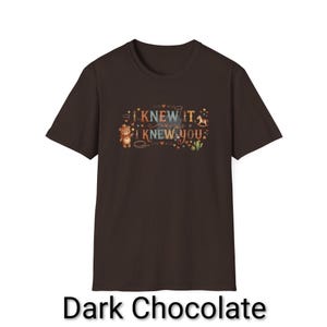 Puede incluir: Una camiseta de manga corta color marr&oacute;n chocolate oscuro con un estampado gr&aacute;fico que incluye el texto I KNEW IT I KNEW YOU. El dise&ntilde;o muestra un peque&ntilde;o oso con sombrero de vaquero, un caballito de madera, un cactus, estrellas y corazones.
