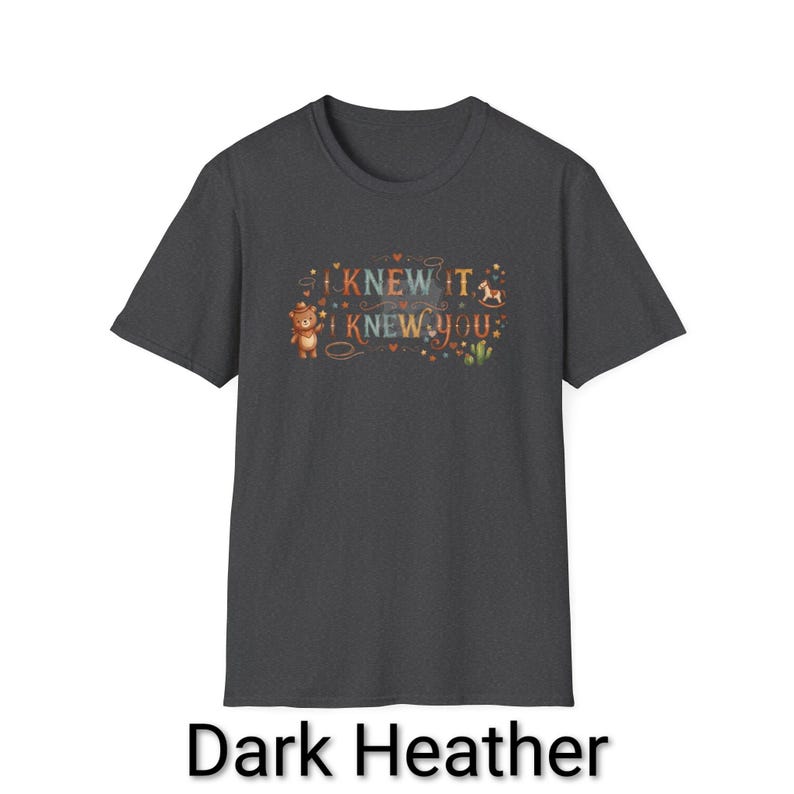Puede incluir: Una camiseta de manga corta en color gris jaspeado oscuro con un estampado gr&aacute;fico que incluye el texto I KNEW IT I KNEW YOU. El dise&ntilde;o muestra un peque&ntilde;o oso marr&oacute;n con sombrero, un caballito de madera, un cactus y estrellas y corazones.
