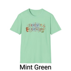 Puede incluir: Una camiseta de manga corta color verde menta con un estampado gr&aacute;fico que incluye el texto I KNEW IT, I KNEW YOU. El dise&ntilde;o presenta un oso marr&oacute;n, un peque&ntilde;o caballito de madera, un cactus y varios corazones y estrellas decorativas.