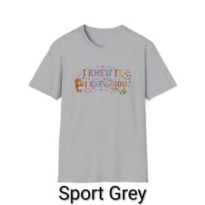 Puede incluir: Una camiseta de manga corta color gris deportivo con un estampado gr&aacute;fico que incluye el texto I KNEW IT, I KNEW YOU. El dise&ntilde;o presenta un peque&ntilde;o oso marr&oacute;n, un caballito de madera, un cactus y varios corazones y estrellas de colores.