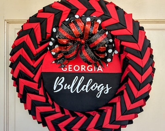 May include: A red and black chevron wreath with a black and white polka dot bow and a sign that reads "GEORGIA Bulldogs".