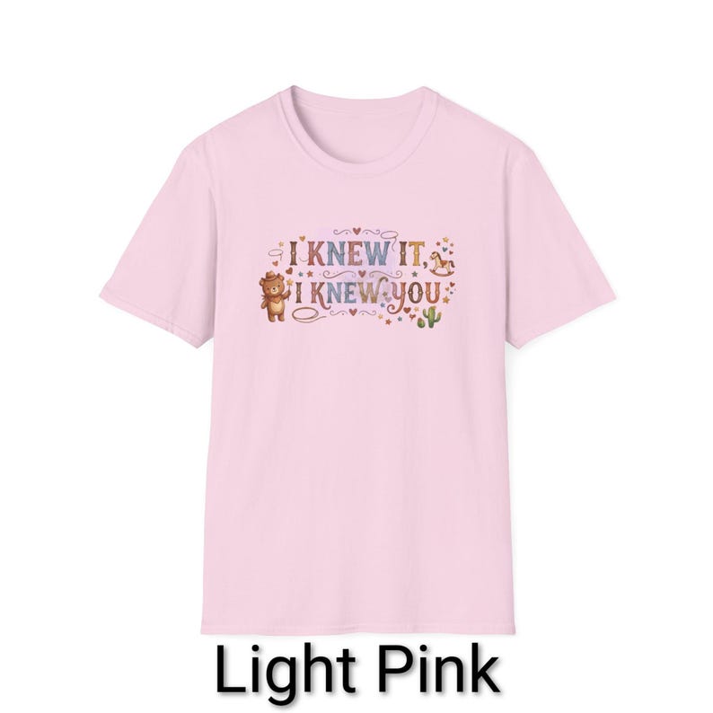 Puede incluir: Una camiseta de manga corta de color rosa claro con un estampado gr&aacute;fico que incluye el texto I KNEW IT, I KNEW YOU. El dise&ntilde;o muestra un oso marr&oacute;n con sombrero, un caballito balanc&iacute;n, un cactus verde y varios corazones y estrellas.