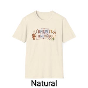 Puede incluir: Una camiseta de manga corta de color natural con un estampado gr&aacute;fico que incluye el texto "I KNEW IT, I KNEW YOU". El dise&ntilde;o presenta un peque&ntilde;o oso marr&oacute;n, un caballito de madera, un cactus y varias estrellas y corazones en tonos tierra.