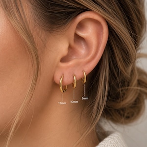 Könnte beinhalten: Drei goldene Creolen in einer Reihe, jede mit einem dünnen, polierten kreisförmigen Design. Gepunktete Linien verbinden die Ringe mit Beschriftungen, die Größen von 12mm, 10mm und 8mm angeben und den abgestuften Durchmesser jedes Ohrrings zeigen.