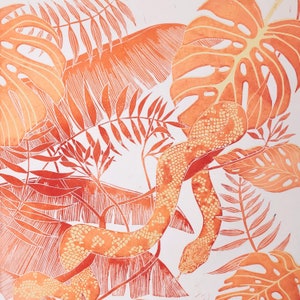 May include: Linocut print in orange and white depicting a snake amidst tropical leaves. The print highlights detailed foliage and a textured snake with a patterned design. The artwork is set against a white background.