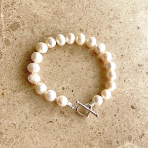 Könnte beinhalten: Ein weißes Perlenarmband mit einem silbernen Toggle-Verschluss.