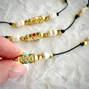 On trend adjustable cord charm necklace with love amulet charm and freshwater cultured pearls. Choice of 3 colours.