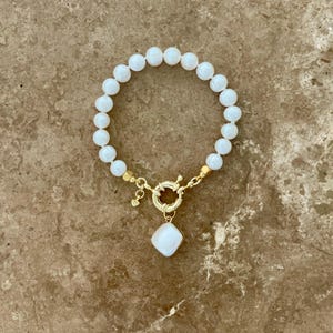K&ouml;nnte beinhalten: Ein wei&szlig;es Perlenarmband mit einem goldenen Verschluss und einem wei&szlig;en Perlenanh&auml;nger.