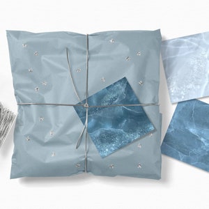 May include: A blue and white gift wrapped in blue tissue paper with silver string and silver stars. The gift is tied with a blue and white marble patterned ribbon.