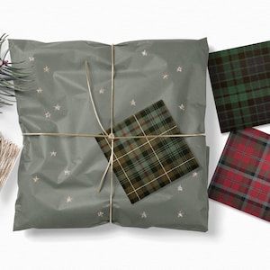May include: A green, brown, and white plaid wrapping paper with gold stars on a gray background. The paper is tied with twine and there are three additional squares of plaid wrapping paper in green, red, and black.