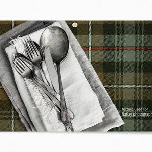 May include: Silverware, including forks and a spoon, are arranged on top of a stack of white and gray linen napkins. The napkins are on a green, brown, and white plaid fabric. The text "texture used for flatlay photography" is in the lower right corner of the image.