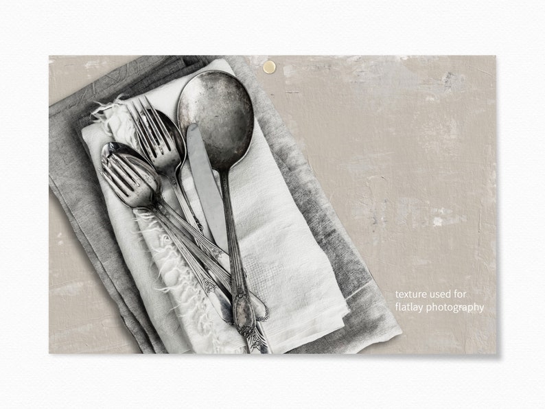 May include: A close-up of a set of silver cutlery, including a fork, knife, and spoon, arranged on a white and gray linen napkin. The cutlery is arranged in a criss-cross pattern, with the knife placed on top of the fork and spoon. The cutlery is slightly tarnished, giving it a vintage look. The background is a light gray, textured surface.  texture used for flatlay photography