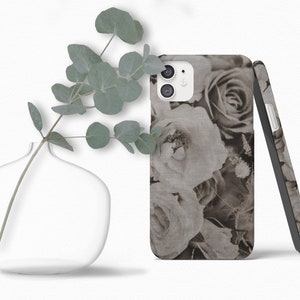 May include: A phone case with a floral design featuring black and white roses. The case is made of a textured material and has a subtle linen look.