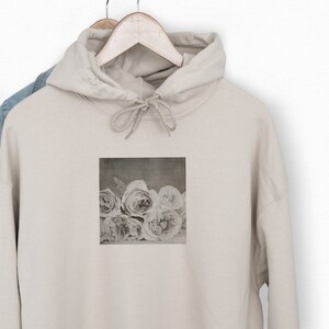 May include: A beige hoodie with a faded image of white roses printed on the front.