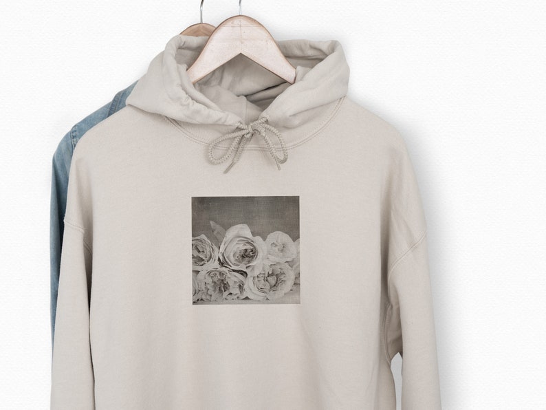 May include: A beige hoodie with a faded image of white roses printed on the front.