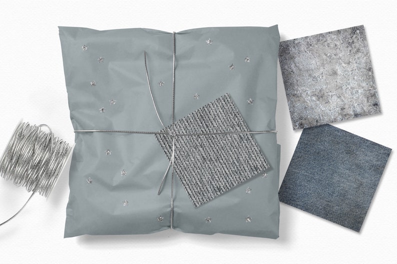 Op de afbeelding: Een grijs cadeau ingepakt in zilverpapier met zilveren sterren en vastgebonden met zilveren touw. Het cadeau ligt op een wit oppervlak. Er zijn drie kleine vierkanten stof op de achtergrond, een is grijs, een is blauw en een is lichtgrijs met een geweven textuur.