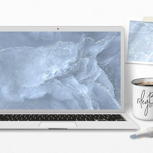 May include: A laptop computer with a blue and silver abstract design on the screen. The laptop is sitting on a white surface with a white mug and a silver marker.