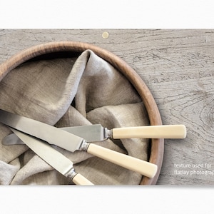 Puede incluir: Tres cuchillos de plata con mangos de marfil est&aacute;n dispuestos en un cuenco de madera forrado con un pa&ntilde;o de lino beige. El cuenco est&aacute; sobre una superficie de madera gris claro. "textura utilizada para la fotograf&iacute;a de plano" est&aacute; escrito en blanco en la esquina inferior derecha de la imagen.