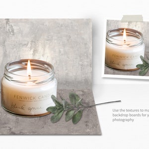 May include: A white candle in a clear glass jar with a gold lid. The candle is lit and the flame is visible. The jar has a label that reads "FENWICK CANDLES" and "black spruce". There is a sprig of green leaves next to the candle.