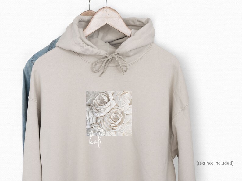 Puede incluir: Una sudadera con capucha beige con un dise&ntilde;o floral blanco y el texto "the half" impreso en la parte delantera.