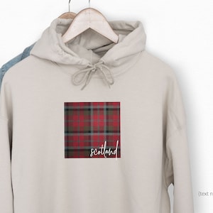 May include: A beige hoodie with a red and black plaid pattern and the word "Scotland" printed on the front.
