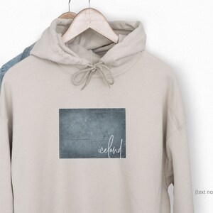 May include: A beige hoodie with a blue and gray textured rectangle graphic and the word "iceland" written in white script.