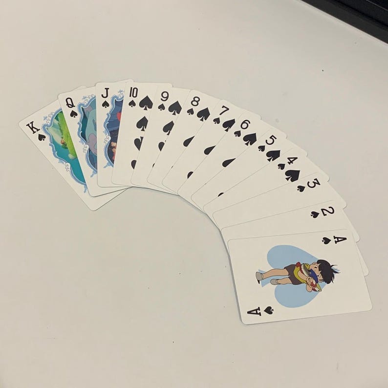 May include: A fan of playing cards featuring the suits of spades and hearts. The cards display the numbers 2 through 10, Jack, Queen, and King of Spades. The Ace of Hearts features an illustration of two characters. The cards are white with black symbols.