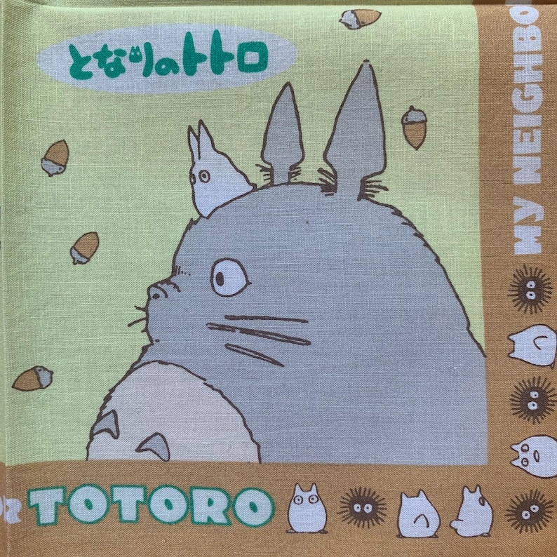 K&ouml;nnte beinhalten: Quadratischer, hellgr&uuml;ner und beigefarbener Stoff mit der Figur Totoro aus dem Zeichentrickfilm Mein Nachbar Totoro. Das Bild enth&auml;lt den japanischen Text "となりのトトロ" und das Wort "TOTORO". Eicheln und andere Charaktere sind ebenfalls zu sehen.