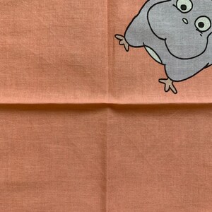 May include: A peach-colored square cloth with a cartoon owl design in the upper right corner. The owl is gray with black eyes and a white outline. The cloth has a textured appearance.
