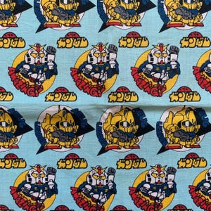 May include: Light blue fabric featuring a repeating pattern of cartoon robots in yellow, white, blue, and red. Each robot is set within a yellow circle with the word "AMAZING" in red. Japanese text is also present.