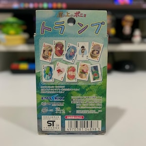 May include: A deck of playing cards featuring illustrations from the animated film "Ponyo". The box is predominantly blue and green, with Japanese text and images of the cards displayed. The cards feature various characters and scenes.