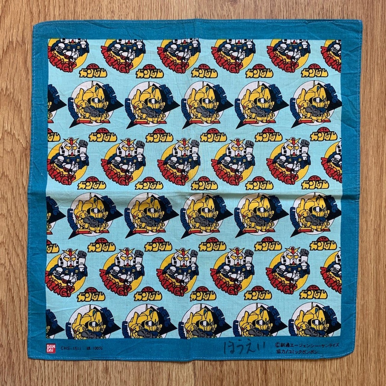 May include: A light blue square handkerchief with a repeating pattern of yellow, red, and white robot illustrations. The border is a darker shade of blue. Japanese text is visible.