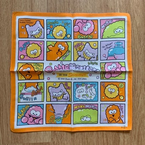 Op de afbeelding: Een kleurrijk katoenen bandana met een cartoonontwerp met verschillende personages met namen met een bubbelthema. De bandana heeft een oranje rand en bevat de tekst "Bubble Trouble!" en "In the Summer".