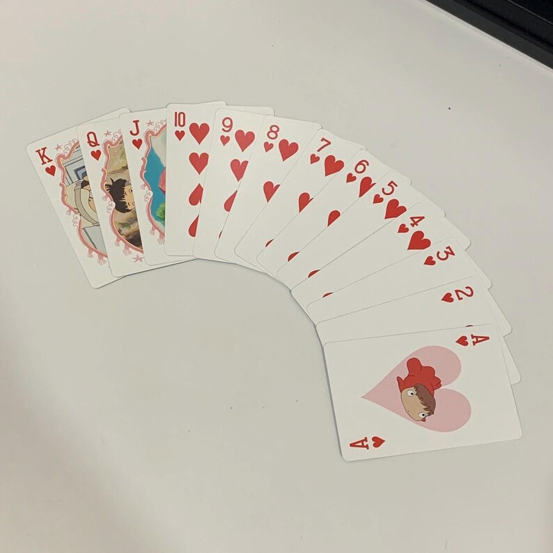 May include: A deck of playing cards fanned out on a white surface. The cards feature red hearts and illustrations of characters. The suits include hearts, with the Ace, 2 through 10, Jack, Queen, and King visible.