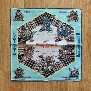 Könnte beinhalten: Ein hellblaues quadratisches Taschentuch mit dem Barcode Battler II Logo und verschiedenen Zeichentrickfiguren in Rüstung. Das Design enthält ein zentrales hexagonales Strichcodemuster, japanischen Text und Namen wie CC-DOLTE und DTH-CAMEL.