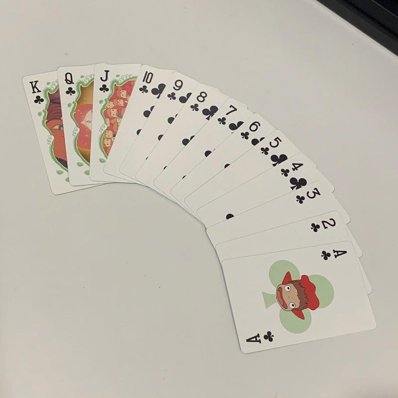May include: A fan of playing cards featuring a unique design. The cards are white with black suit symbols and numbers. The face cards have colorful illustrations. The Ace of Clubs features a cartoon character. The cards are arranged in a semi-circle.