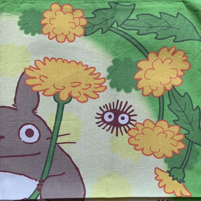 May include: A green and yellow patterned fabric featuring a cartoon character holding a large yellow flower. The design includes yellow dandelions, green leaves, and a small, round, spiky creature with large eyes. The fabric has a light green and yellow background.