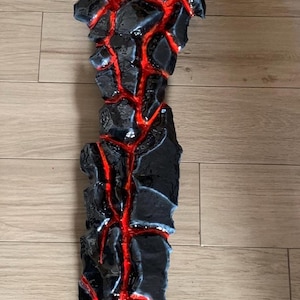May include: A black and red sword with a gold handle. The blade is made to look like lava rock with red veins running through it.