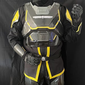 May include: A full-body black and yellow futuristic armor suit. The helmet, chest plate, and leg armor have yellow accents. The suit includes a helmet with a visor, a chest plate with a skull emblem, and gloves. The armor is designed for cosplay or costume use.