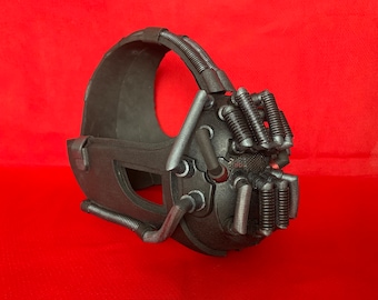May include: A black face mask featuring a textured finish, a wide head strap, and multiple silver-toned ribbed tubes extending from the front section. The mask includes a mesh-covered mouth area and rigid structural components along the sides.