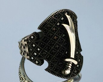 May include: A silver ring with a black stone design and a silver sword motif.