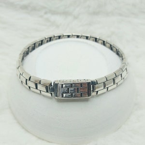 May include: A silver bracelet with a rectangular, patterned clasp. The bracelet is made of linked, rectangular pieces.