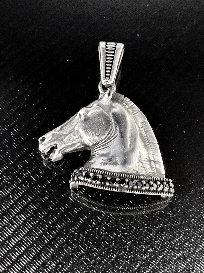 May include: Silver horse head pendant with black gemstone accents. The pendant has a detailed design and a textured surface.