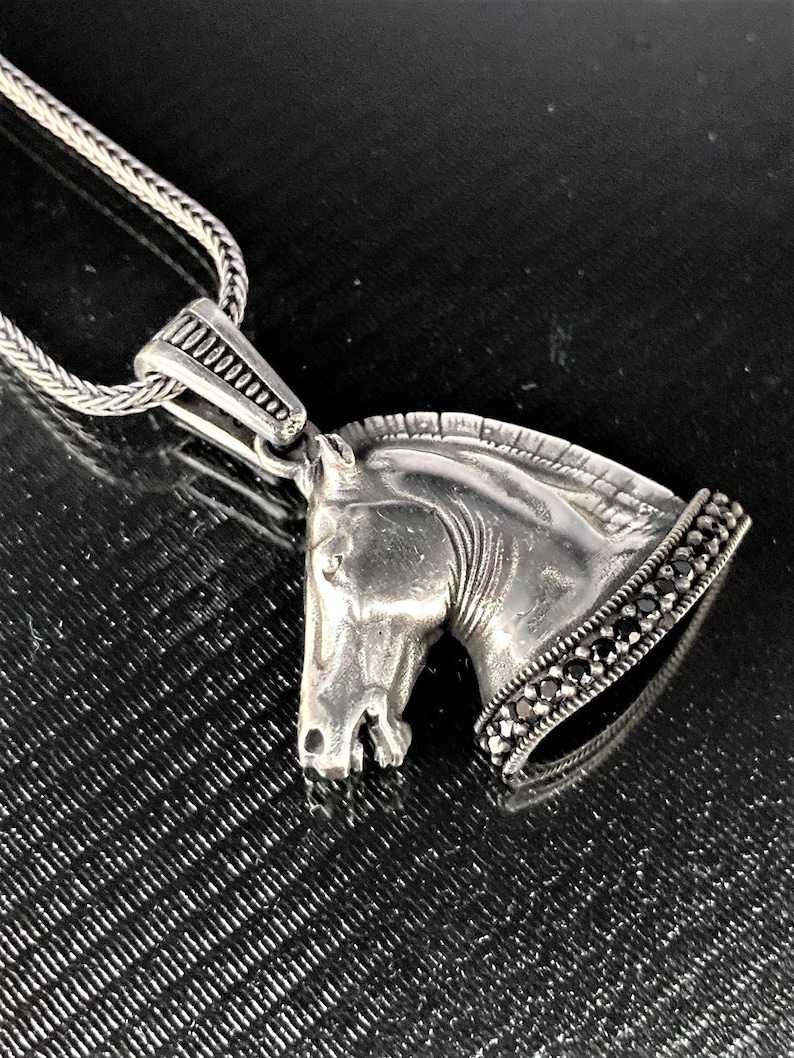 May include: A silver horse head pendant necklace with black gemstones around the base. The chain is silver and has a braided design.