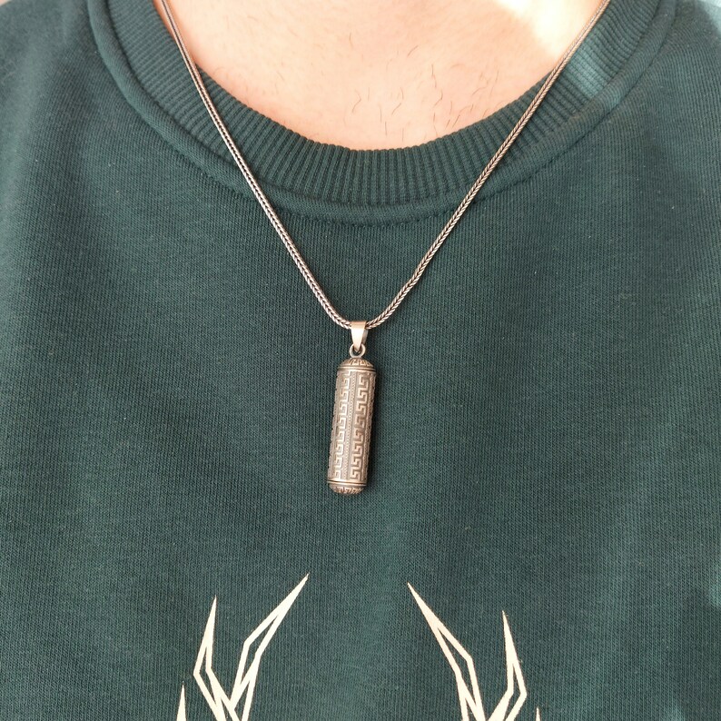 May include: A silver chain necklace with a silver pendant. The pendant is a cylinder with a geometric pattern.