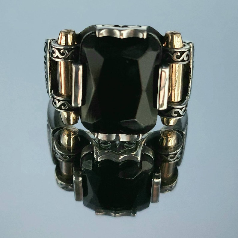 May include: A silver ring with a black gemstone and gold accents. The ring has a detailed design with intricate scrollwork.