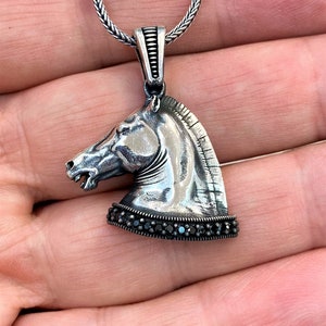 May include: Silver horse head pendant necklace with black gemstone accents. The pendant is detailed with a textured finish and a chain link necklace.